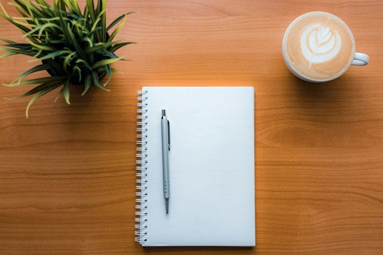 Notebook, coffee and plant on desk symbolising calm reflection and early awareness of burnout