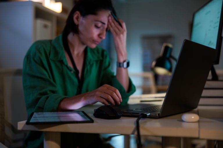 Person sitting at desk feeling tired and stressed while working late — illustrating the difference between stress and burnout.
